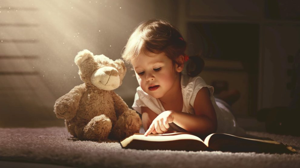 Child reading a book with a teddy bear
